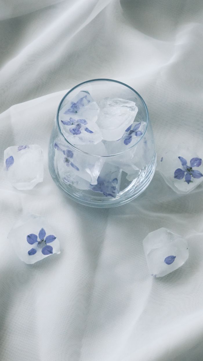 Home Glass with floral ice cubes on soft, white fabric. Perfect for refreshing, aesthetic themes.