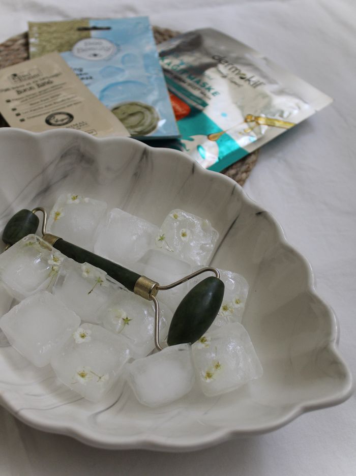 Home A jade roller on ice cubes and skincare products in a marble dish, ideal for beauty routines.